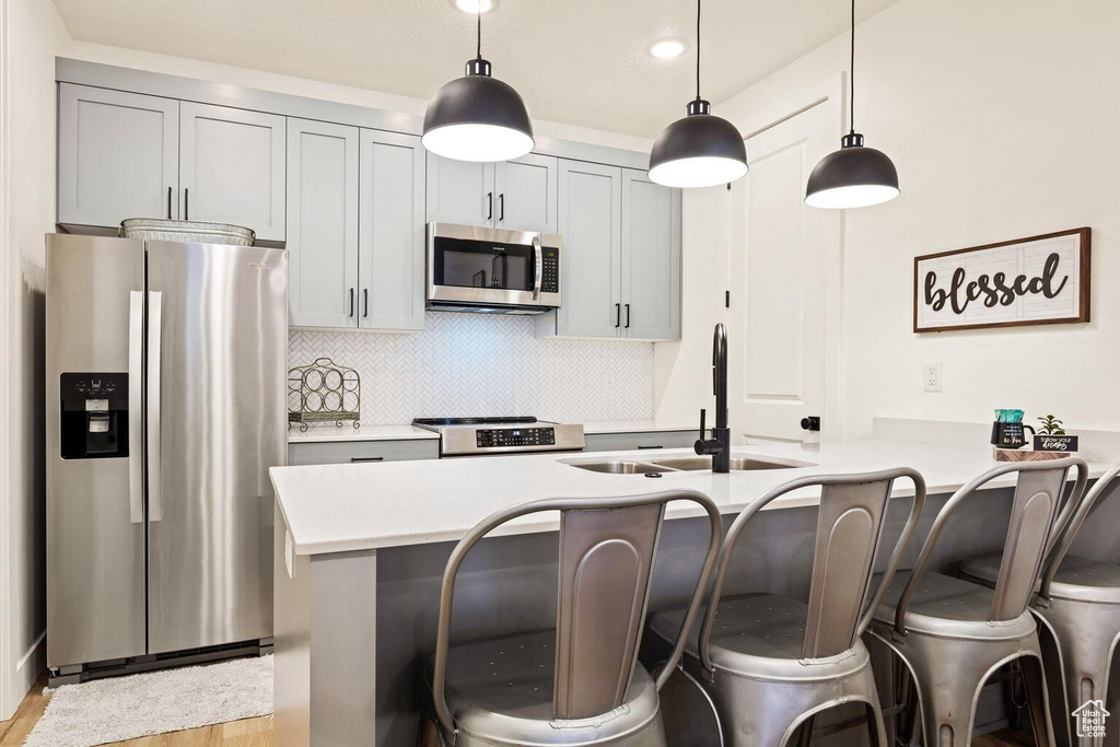 Kitchen with pendant lighting, light hardwood / wood-style flooring, tasteful backsplash, and appliances with stainless steel finishes
