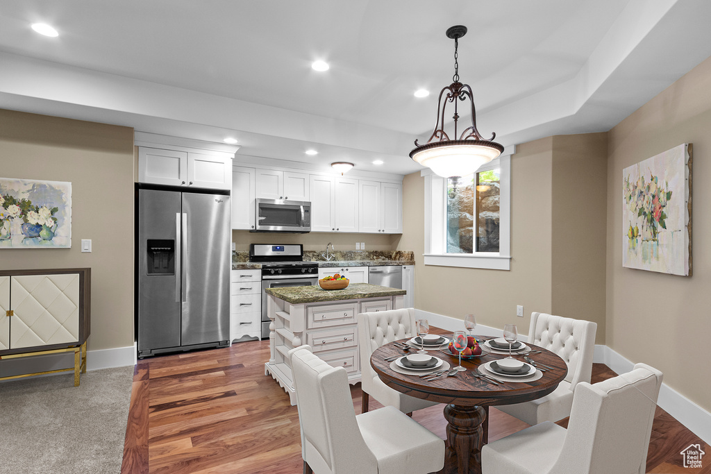Kitchen with stainless steel appliances, pendant lighting, dark colored carpet, white cabinets, and a center island