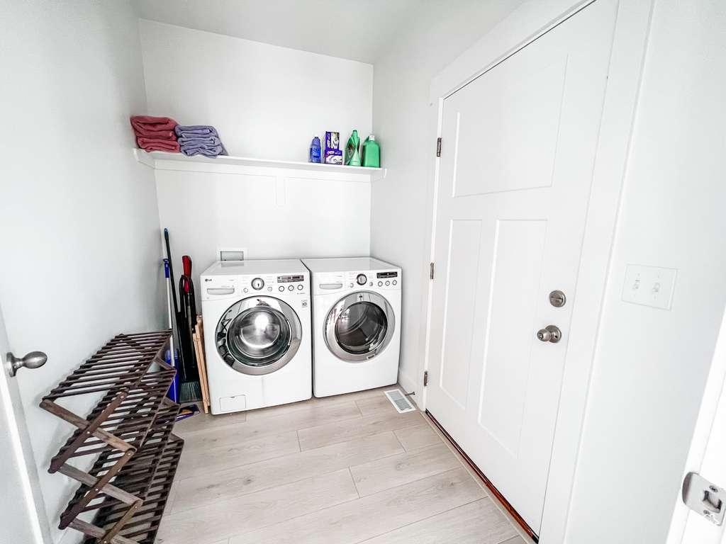 Laundry area featuring washing machine and clothes dryer and light hardwood / wood-style flooring
