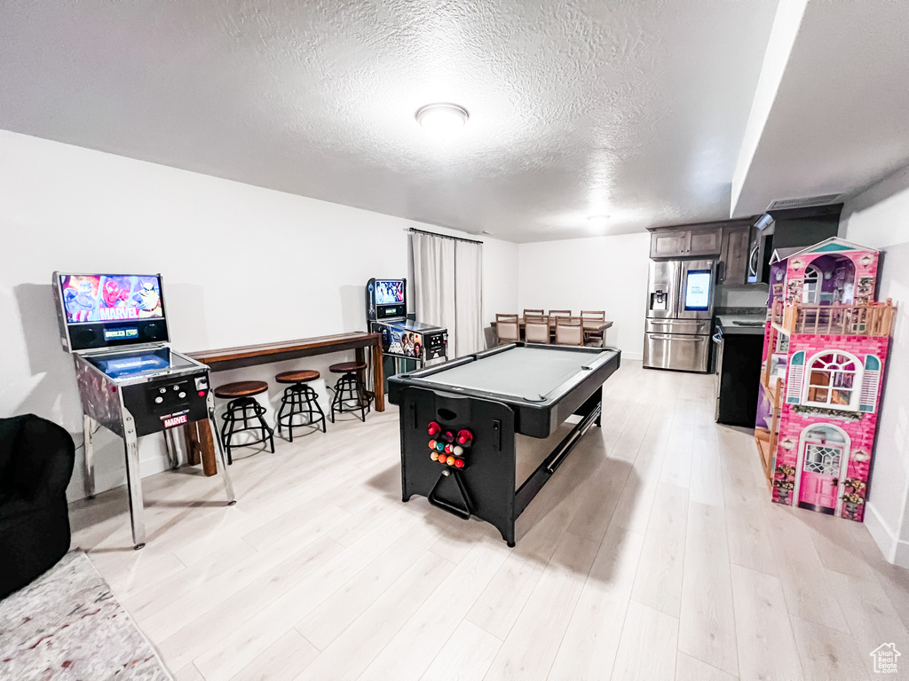 Game room with light wood-type flooring, a textured ceiling, and pool table