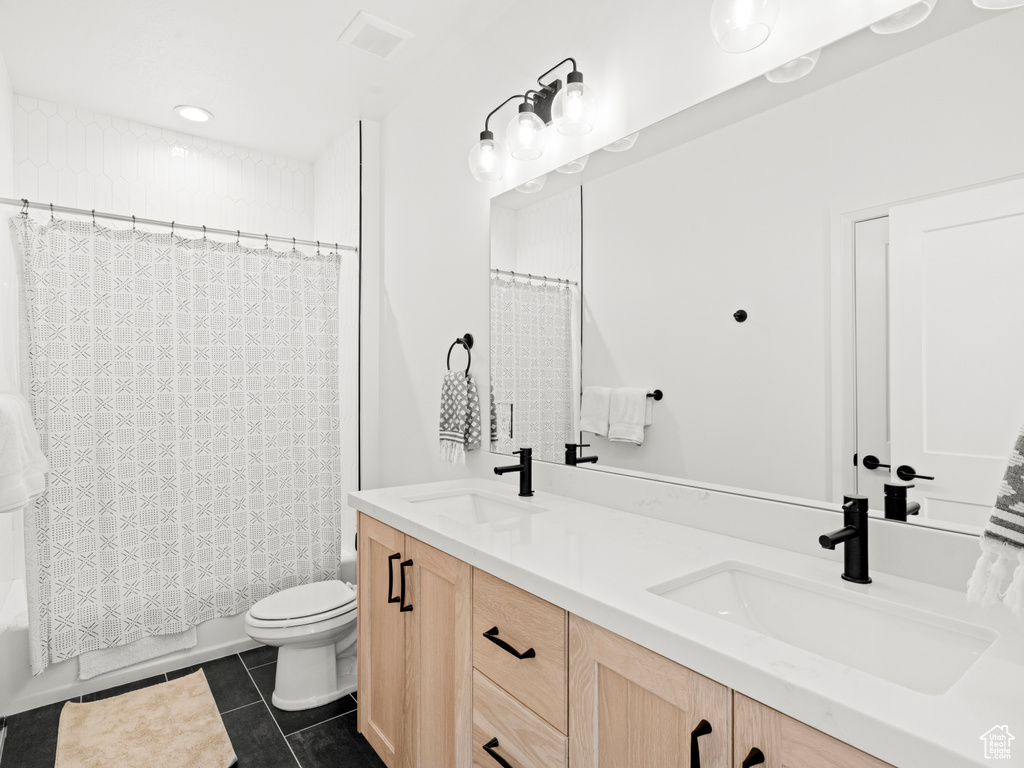 Full bathroom with tile floors, double sink vanity, toilet, and shower / bath combo with shower curtain