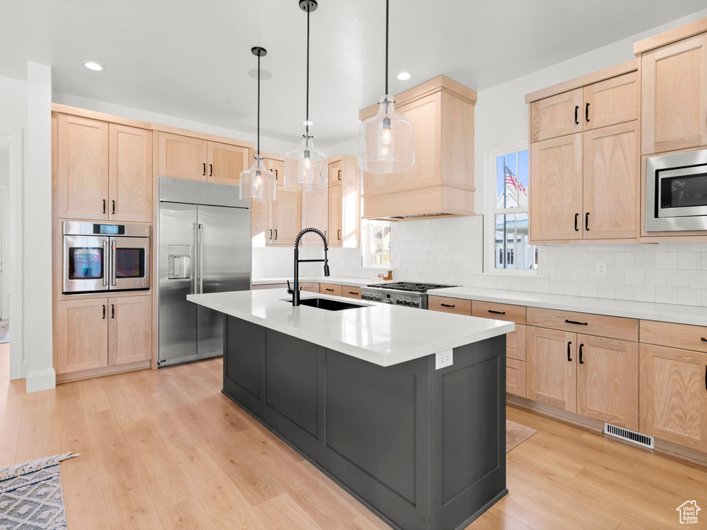 Kitchen with built in appliances, backsplash, light hardwood / wood-style flooring, a center island with sink, and sink