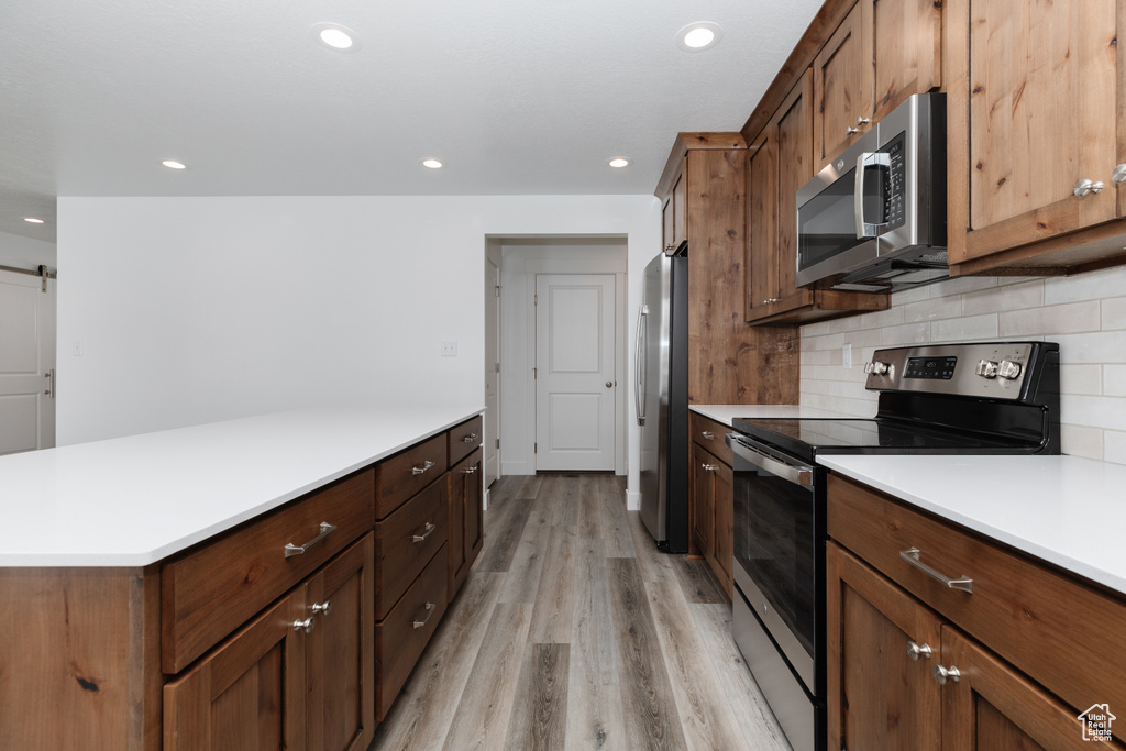 Kitchen with light wood-type flooring, stainless steel appliances, and backsplash