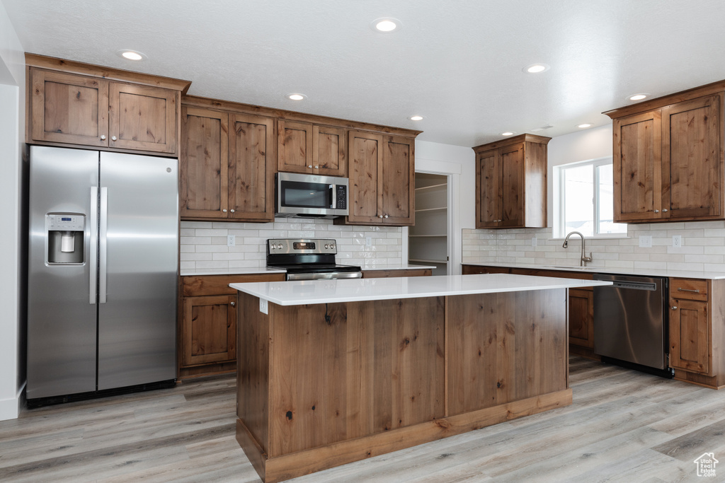 Kitchen featuring light hardwood / wood-style floors, appliances with stainless steel finishes, a center island, and backsplash