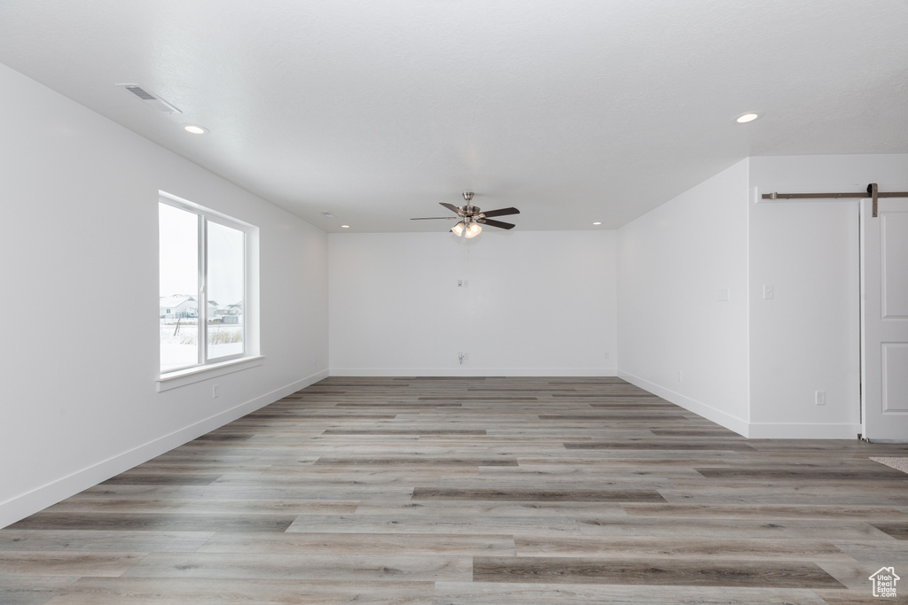 Unfurnished room with light hardwood / wood-style floors, a barn door, and ceiling fan