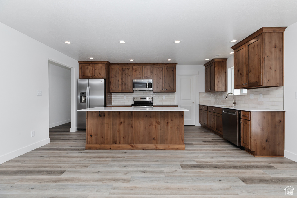Kitchen with a center island, tasteful backsplash, light hardwood / wood-style flooring, and appliances with stainless steel finishes