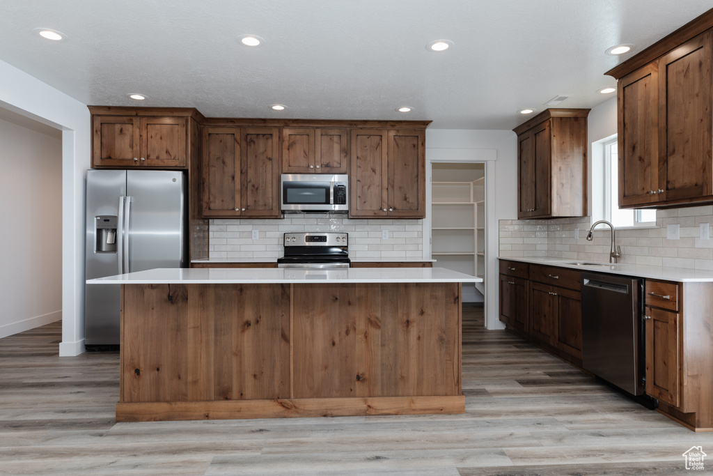 Kitchen featuring stainless steel appliances, a center island, light hardwood / wood-style flooring, and backsplash
