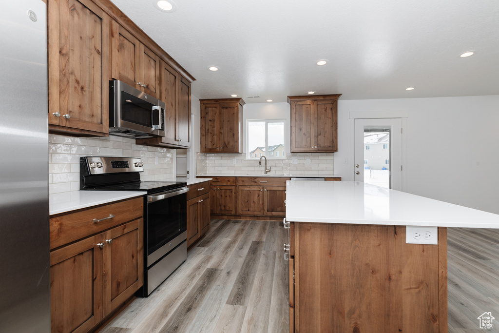Kitchen with appliances with stainless steel finishes, a kitchen island, backsplash, sink, and light wood-type flooring