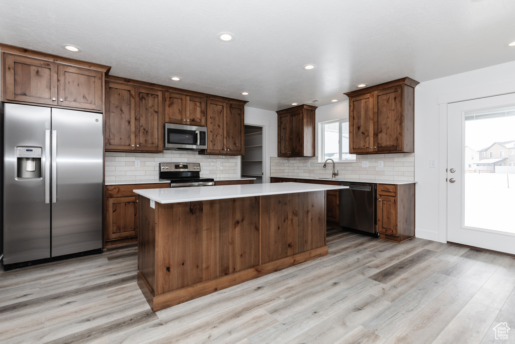 Kitchen featuring light hardwood / wood-style flooring, a kitchen island, appliances with stainless steel finishes, and backsplash