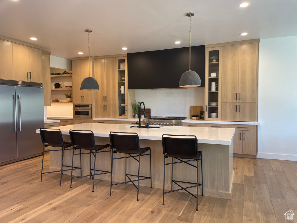 Kitchen with a center island with sink, light hardwood / wood-style floors, stainless steel appliances, and decorative light fixtures