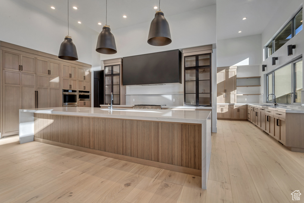 Kitchen with pendant lighting, light wood-type flooring, stainless steel oven, a high ceiling, and a kitchen island with sink