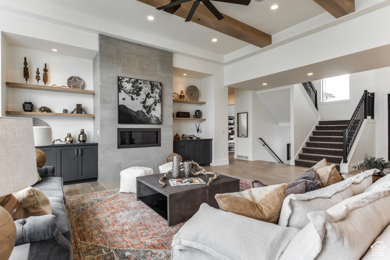 Living room with ceiling fan, hardwood / wood-style floors, built in features, beamed ceiling, and a fireplace