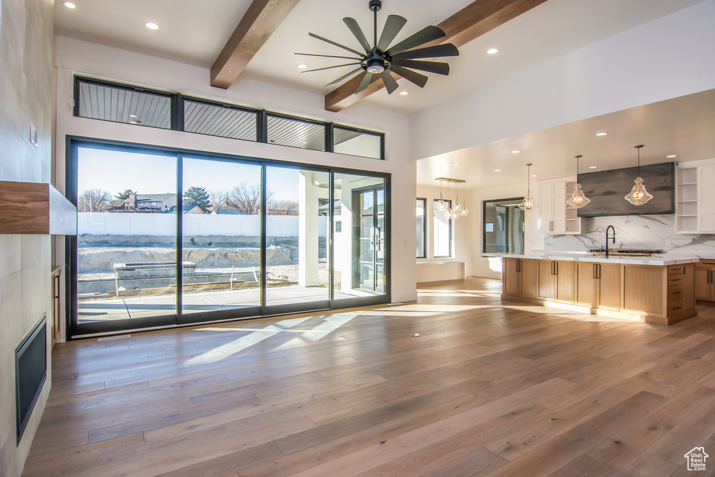 Unfurnished living room with wood-type flooring, plenty of natural light, beamed ceiling, and ceiling fan with notable chandelier