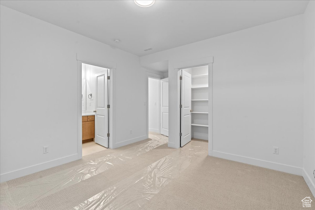 Unfurnished bedroom with a closet, ensuite bathroom, light colored carpet, and a walk in closet