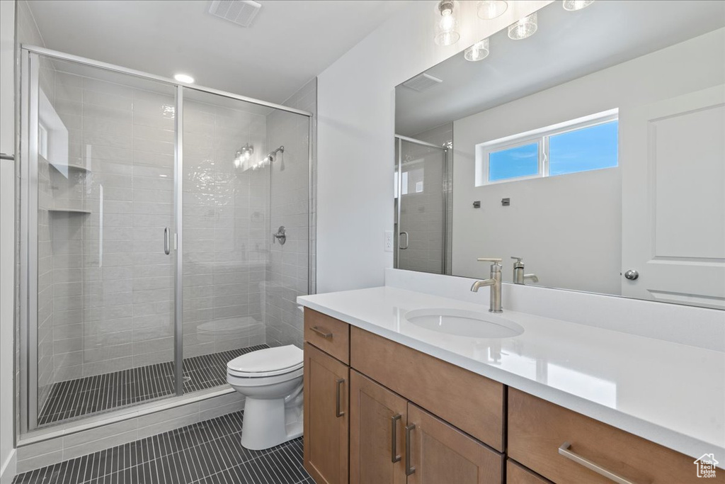 Bathroom featuring a shower with door, vanity, tile patterned floors, and toilet