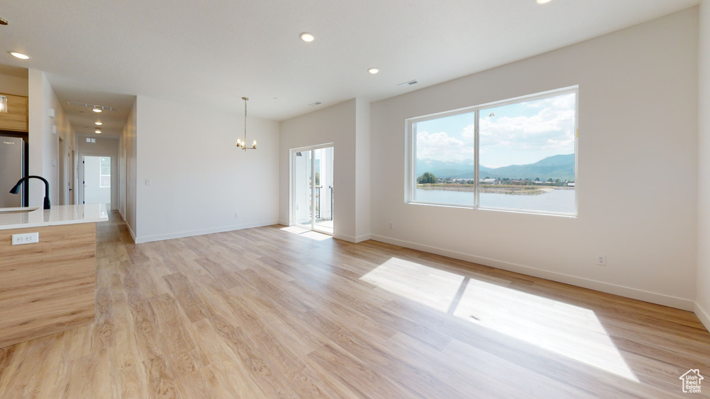 Unfurnished living room featuring a water and mountain view, a chandelier, sink, and light hardwood / wood-style floors
