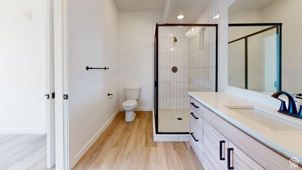 Bathroom featuring wood-type flooring, vanity, toilet, and a shower with door