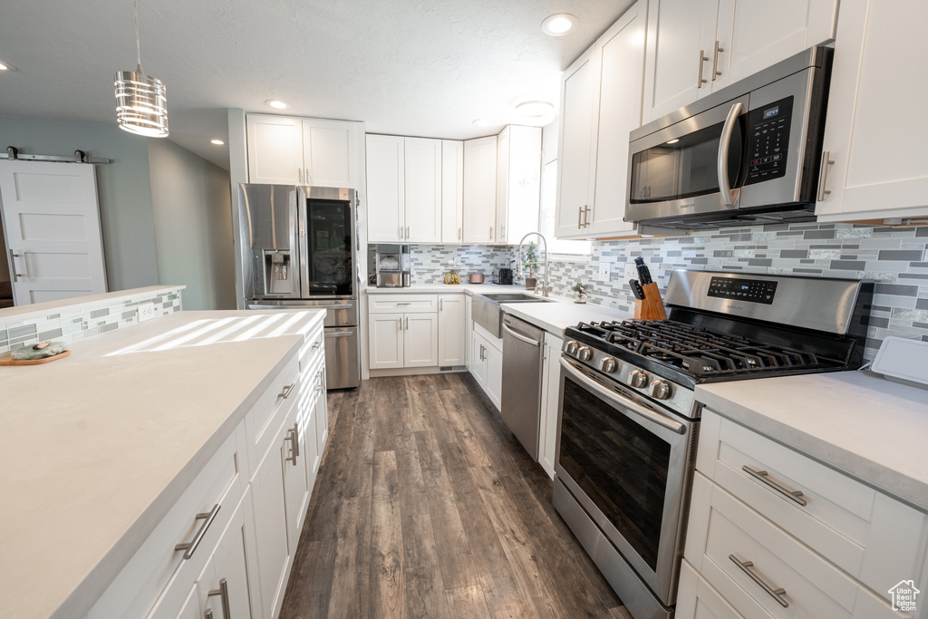 Kitchen featuring decorative light fixtures, stainless steel appliances, backsplash, dark hardwood / wood-style floors, and white cabinetry