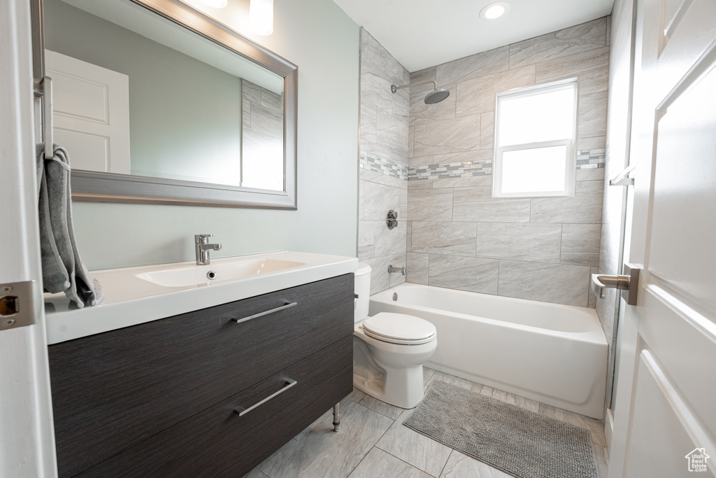 Full bathroom with toilet, tiled shower / bath combo, vanity with extensive cabinet space, and tile flooring