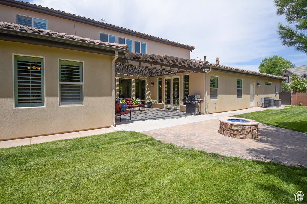 Rear view of property featuring a pergola, a patio, central AC unit, an outdoor fire pit, and a lawn