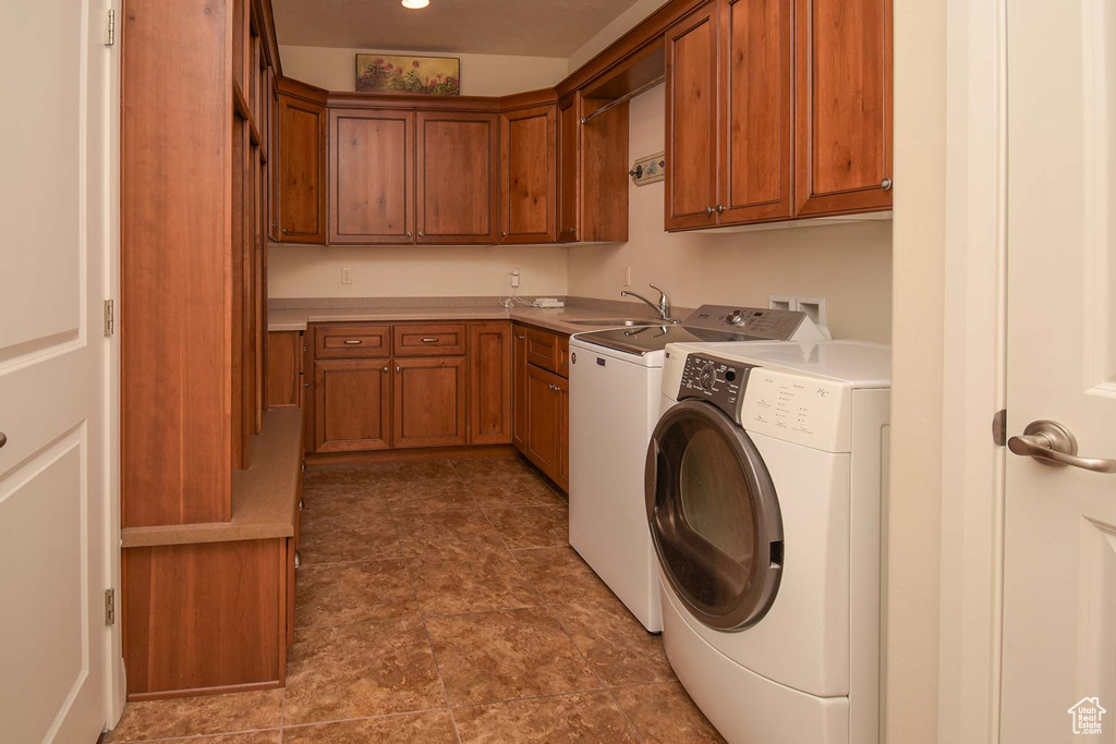 Laundry area with washing machine and clothes dryer, sink, cabinets, and dark tile flooring