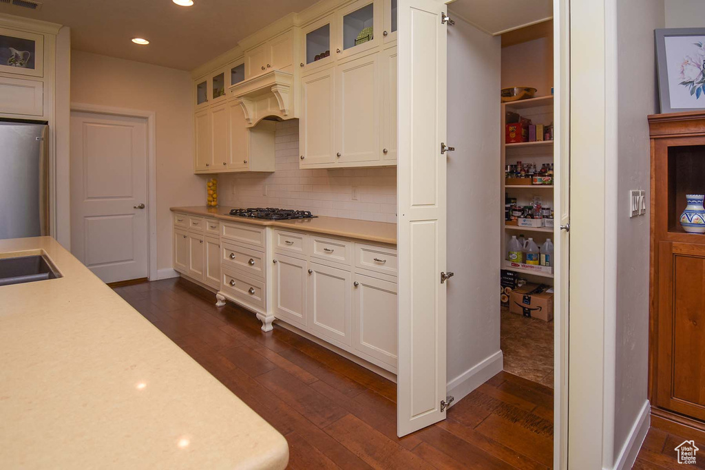 Kitchen featuring dark hardwood / wood-style flooring, white cabinets, stainless steel gas cooktop, backsplash, and refrigerator