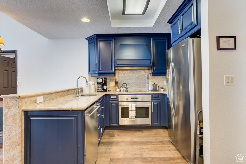 Kitchen with light hardwood / wood-style floors, appliances with stainless steel finishes, premium range hood, sink, and blue cabinetry