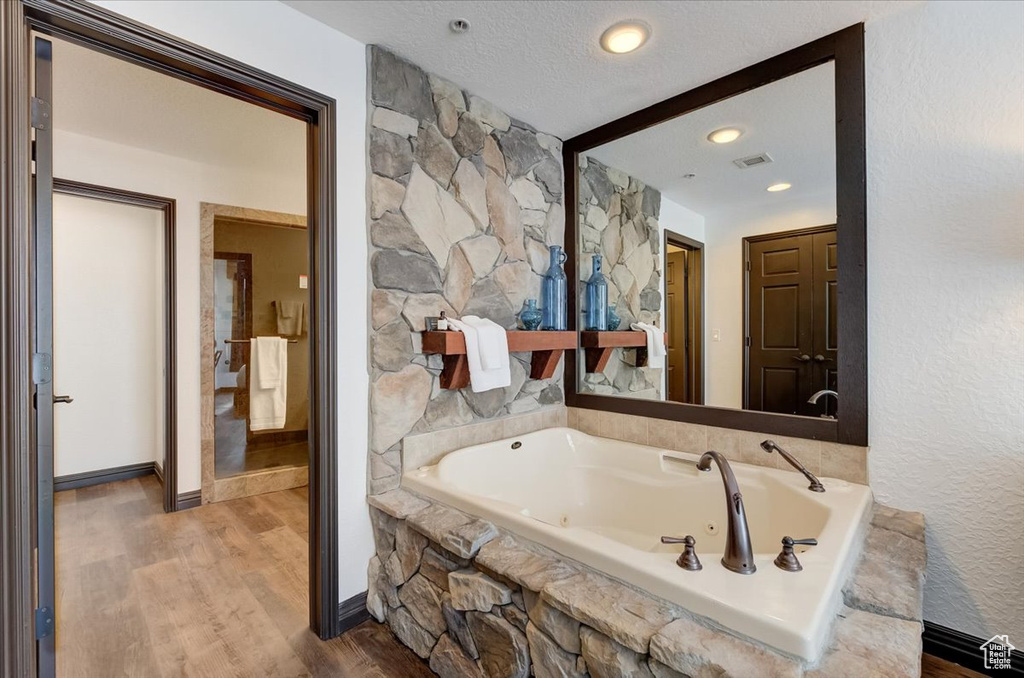 Bathroom with a textured ceiling, tiled bath, and hardwood / wood-style flooring