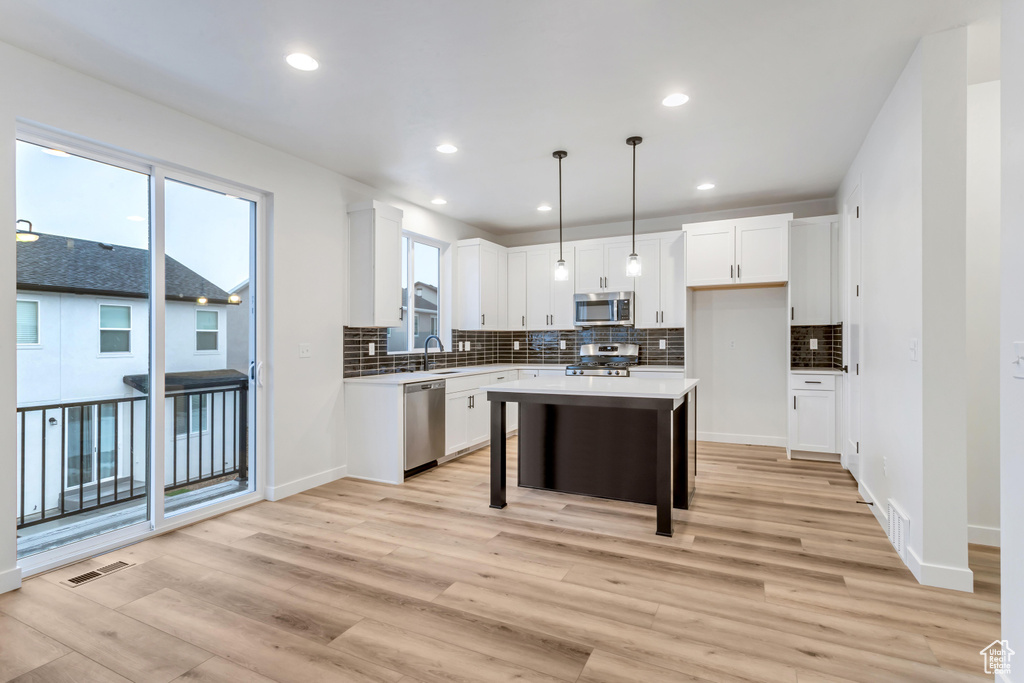 Kitchen with a breakfast bar area, hanging light fixtures, appliances with stainless steel finishes, light hardwood / wood-style flooring, and a kitchen island