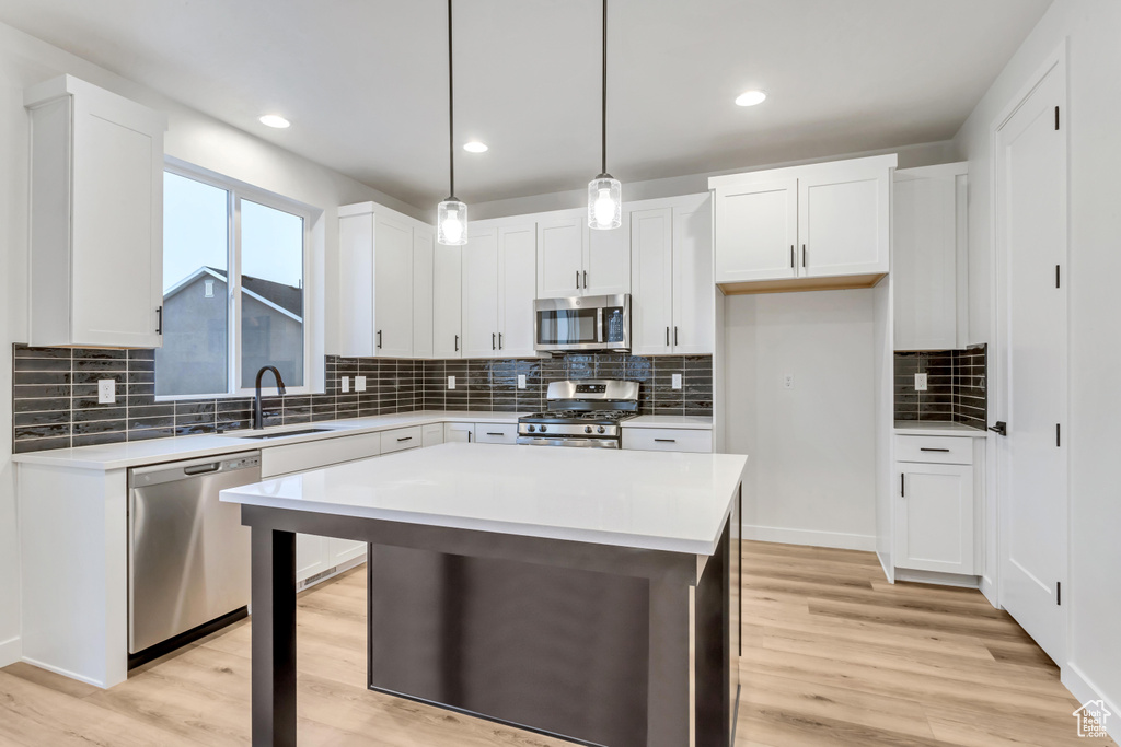Kitchen with appliances with stainless steel finishes, a center island, pendant lighting, sink, and white cabinetry