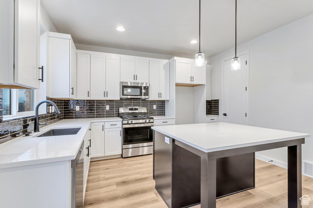Kitchen with hanging light fixtures, stainless steel appliances, light wood-type flooring, sink, and a kitchen island