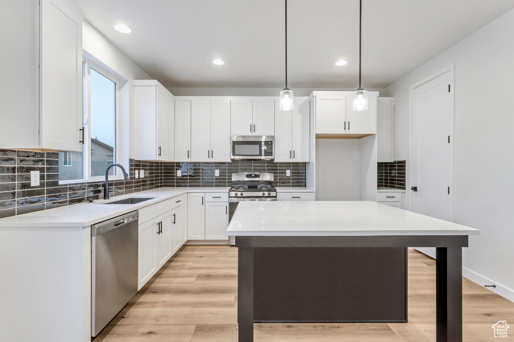 Kitchen featuring a kitchen island, hanging light fixtures, appliances with stainless steel finishes, light hardwood / wood-style flooring, and sink