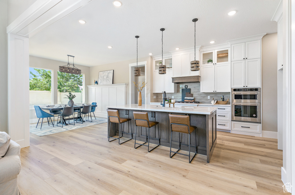 Kitchen featuring hanging light fixtures, stainless steel appliances, a center island with sink, and light hardwood / wood-style flooring