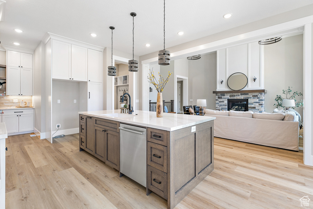 Kitchen featuring light hardwood / wood-style floors, white cabinetry, stainless steel dishwasher, sink, and a fireplace