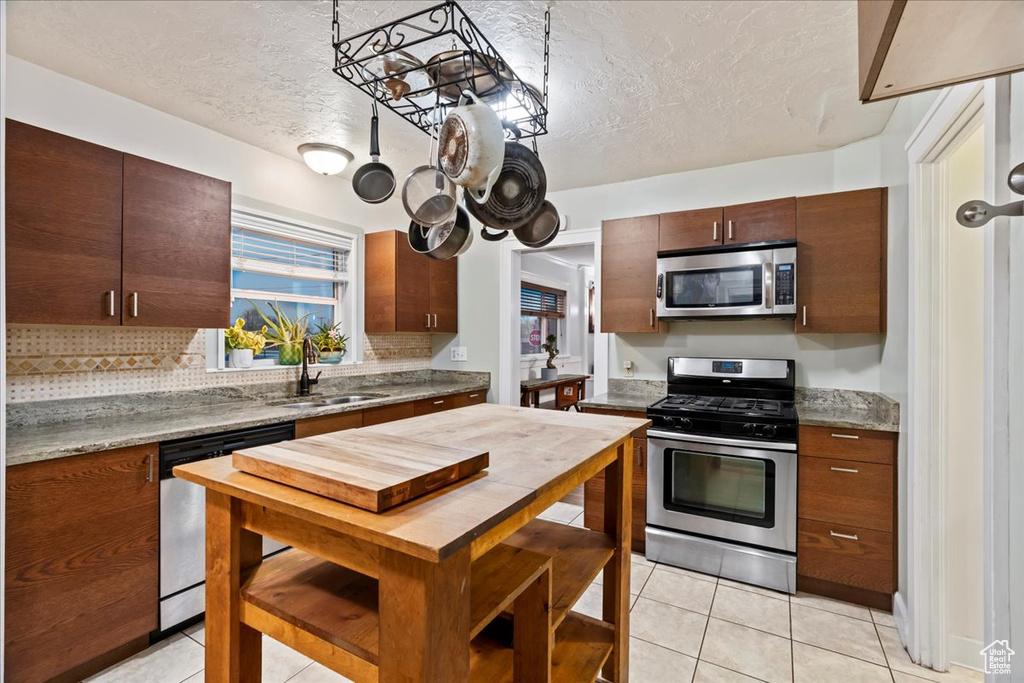 Kitchen featuring a textured ceiling, stainless steel appliances, light tile floors, sink, and tasteful backsplash