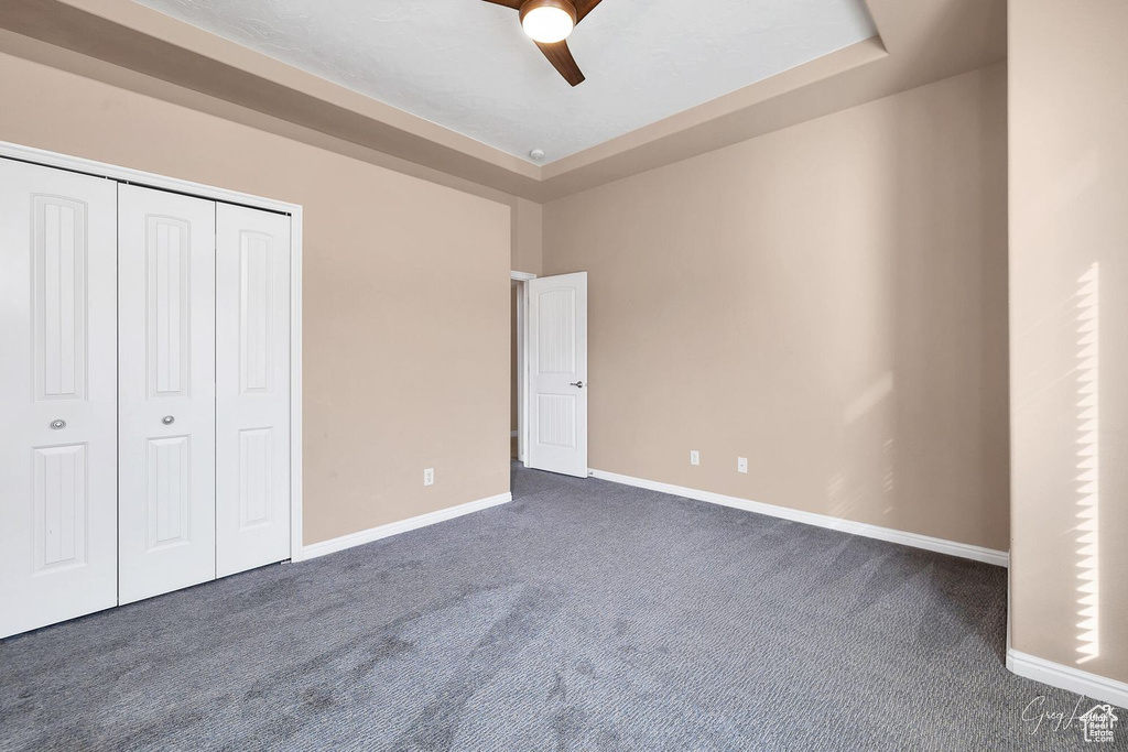 Unfurnished bedroom with dark carpet, a tray ceiling, and ceiling fan