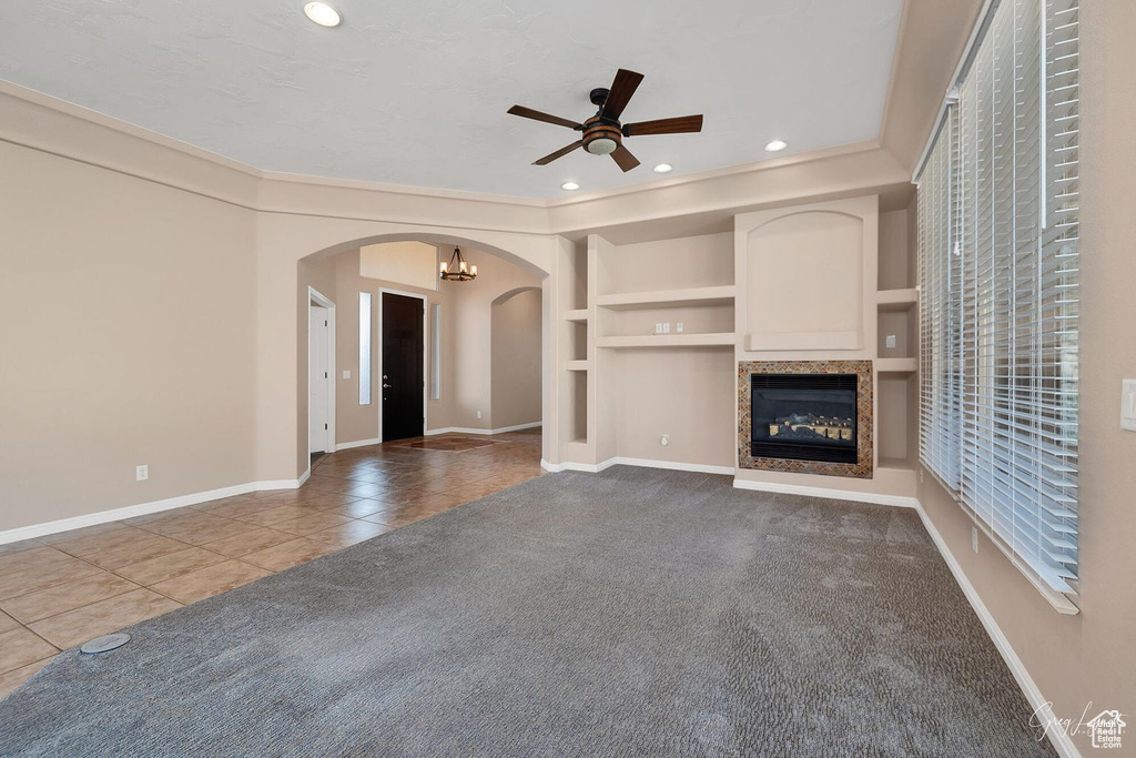Unfurnished living room with ceiling fan with notable chandelier, light tile floors, and built in shelves