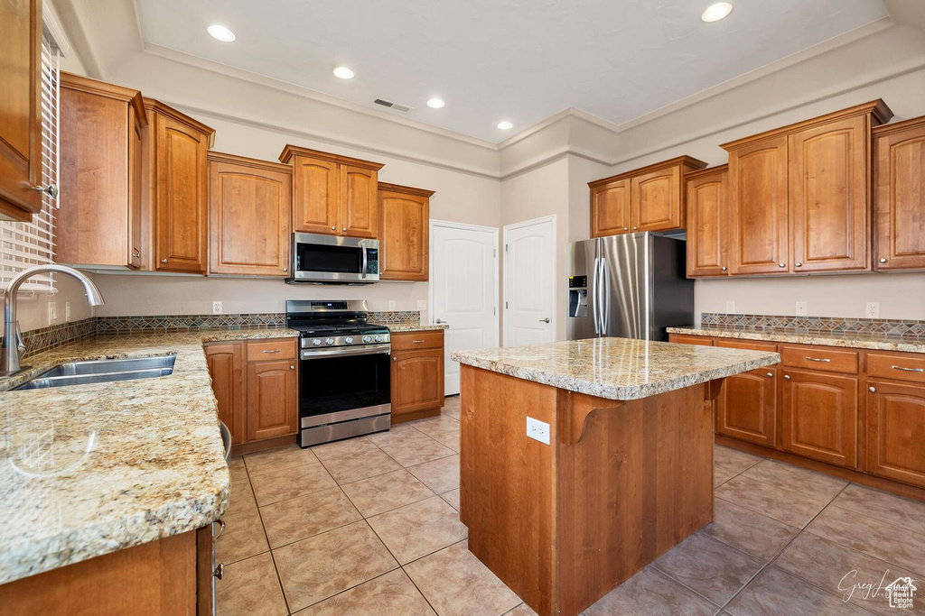 Kitchen with appliances with stainless steel finishes, a center island, light stone counters, light tile floors, and sink