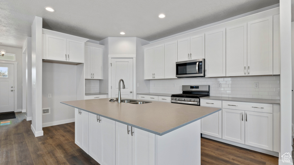 Kitchen featuring dark wood-type flooring, white cabinets, a center island with sink, sink, and stainless steel appliances