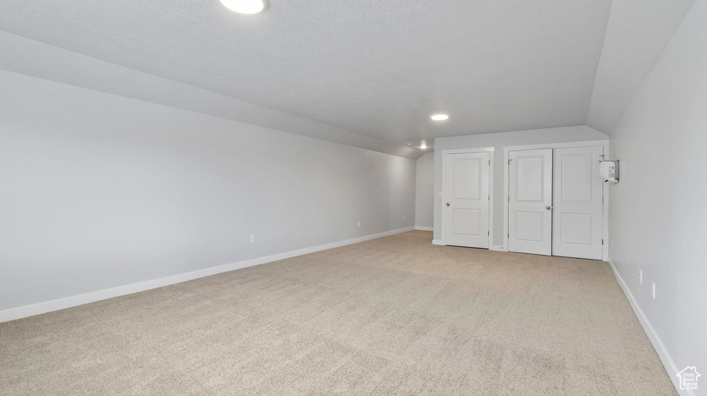 Carpeted empty room with a textured ceiling and lofted ceiling