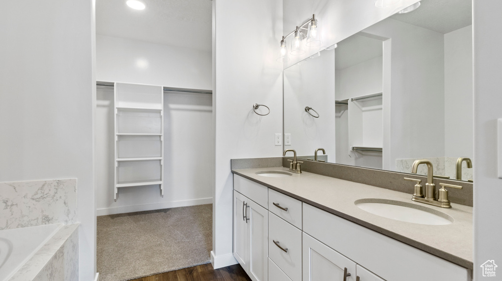 Bathroom with hardwood / wood-style floors, vanity with extensive cabinet space, double sink, and a bath