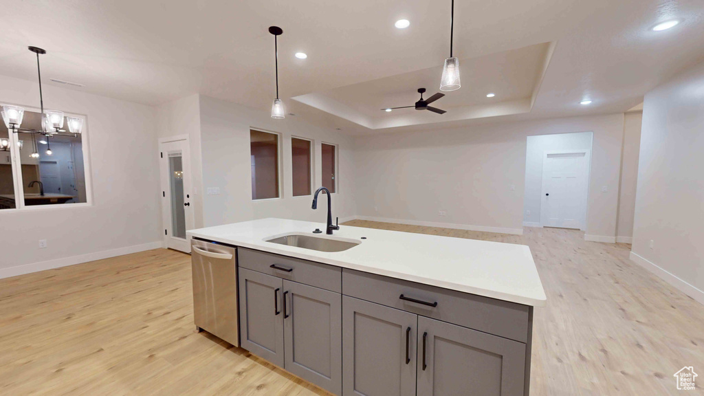 Kitchen featuring a raised ceiling, ceiling fan with notable chandelier, gray cabinets, sink, and stainless steel dishwasher