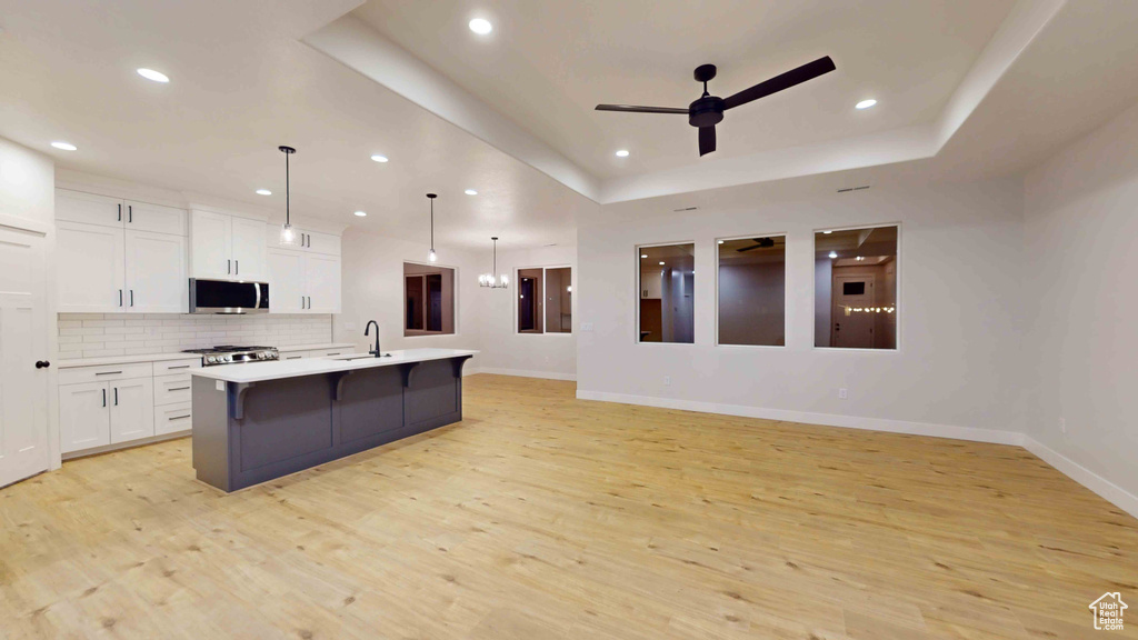 Kitchen featuring an island with sink, pendant lighting, a tray ceiling, and light hardwood / wood-style flooring