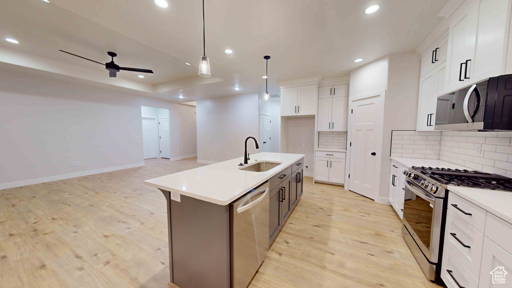 Kitchen with stainless steel appliances, ceiling fan, white cabinetry, sink, and light wood-type flooring