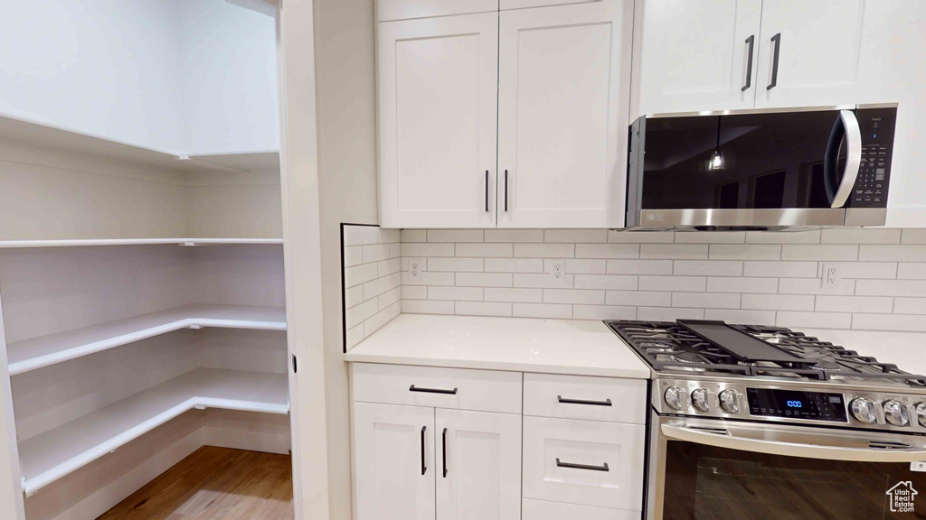 Kitchen with backsplash, white cabinets, stainless steel appliances, and light hardwood / wood-style floors