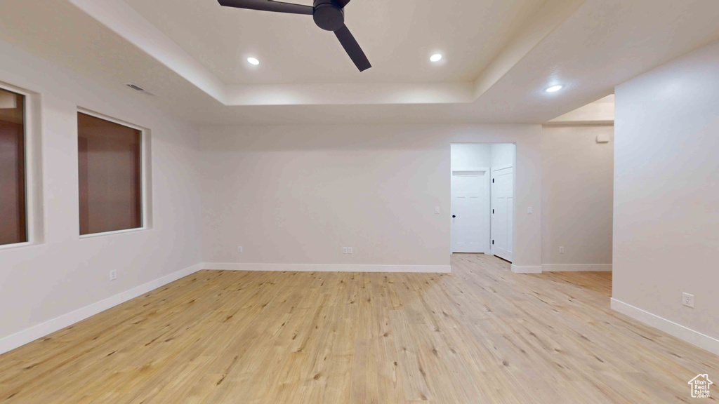 Spare room with light wood-type flooring, ceiling fan, and a raised ceiling