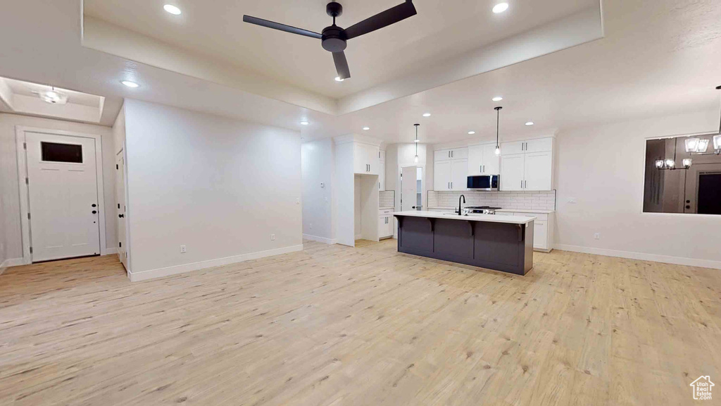 Kitchen with white cabinets, decorative light fixtures, light hardwood / wood-style flooring, and ceiling fan with notable chandelier