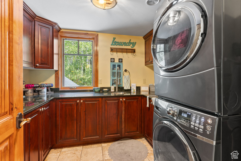 Laundry room with stacked washer / drying machine, light tile floors, cabinets, and sink