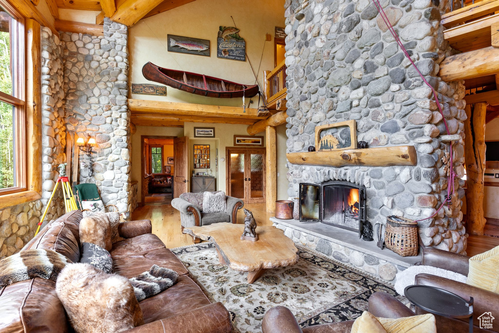 Living room featuring wood-type flooring, a stone fireplace, and beam ceiling