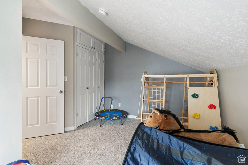 Bedroom featuring vaulted ceiling, light colored carpet, a closet, and a textured ceiling
